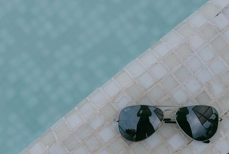Aviator sunglasses resting on the tiled edge of a swimming pool