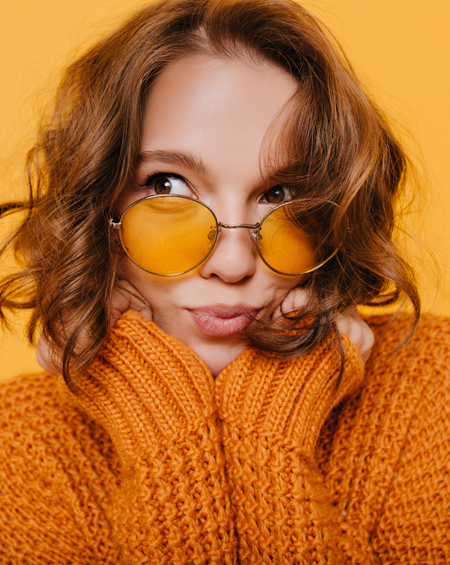 Woman in a knitted orange jumper wearing round amber-tinted glasses