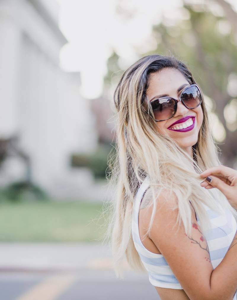 Woman with long blonde hair smiling in oversized dark sunglasses