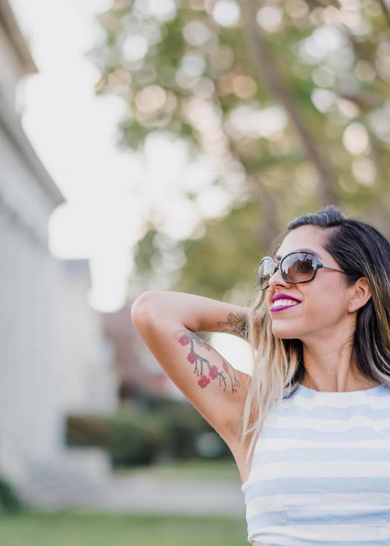 Woman in large sunglasses with one hand behind her head, looking up