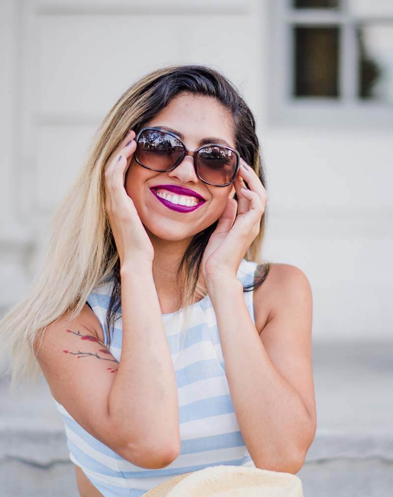 Smiling woman holding a pair of oversized dark sunglasses to her face